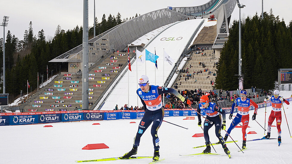 Vier NoKo Athleten beim Langlaufen vor der Skisprungschanze