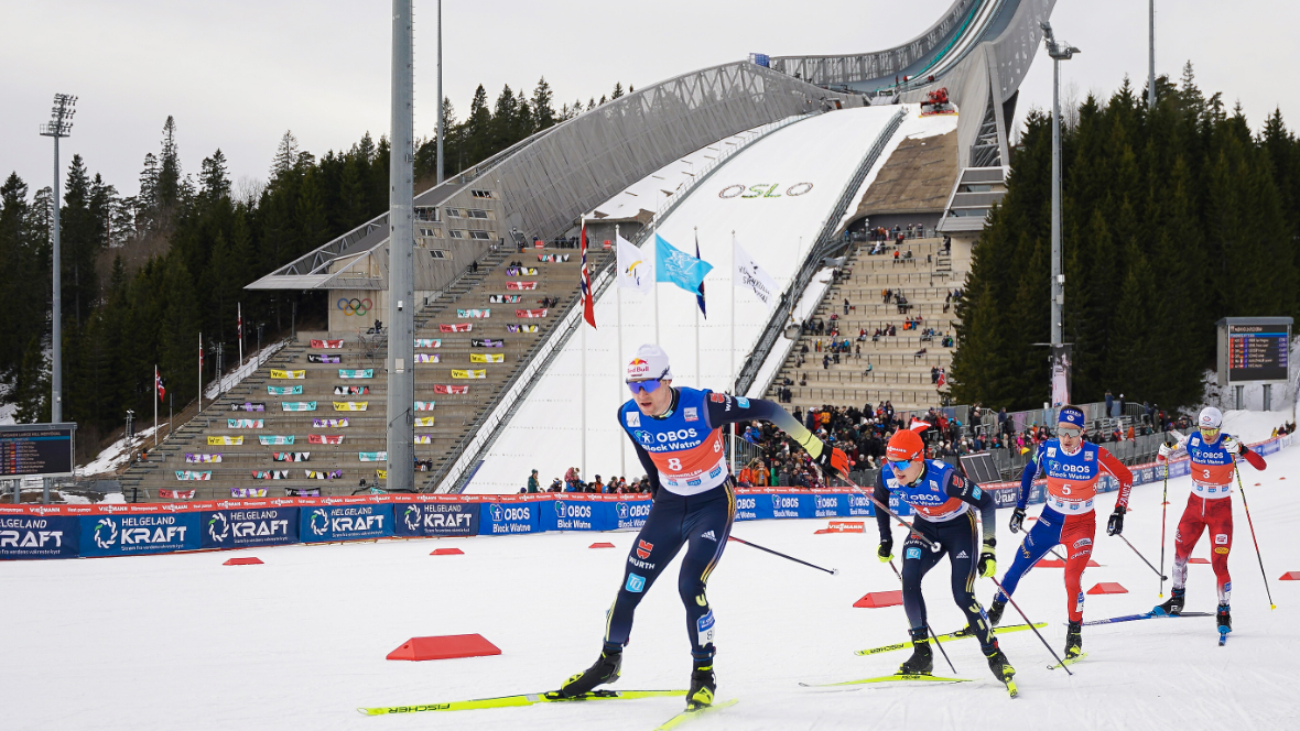 Nordische Kombinierer laufen auf einer Loipe an der Schanze vorbei