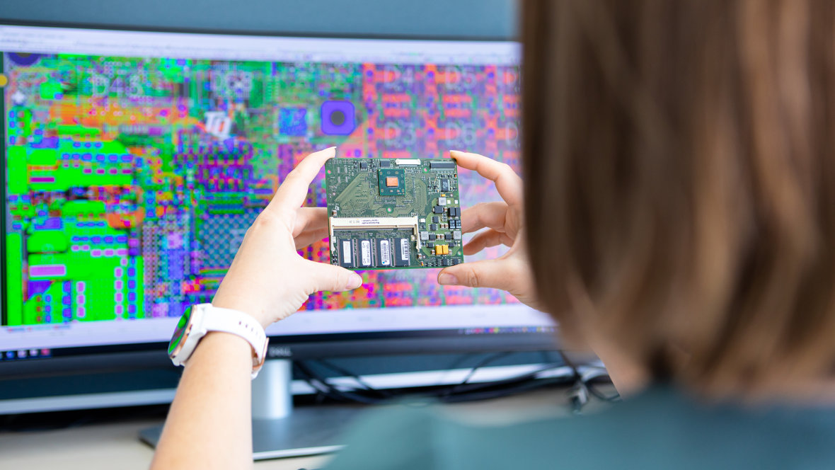 Frau hält eine Leiterplatte vor ihren Monitor